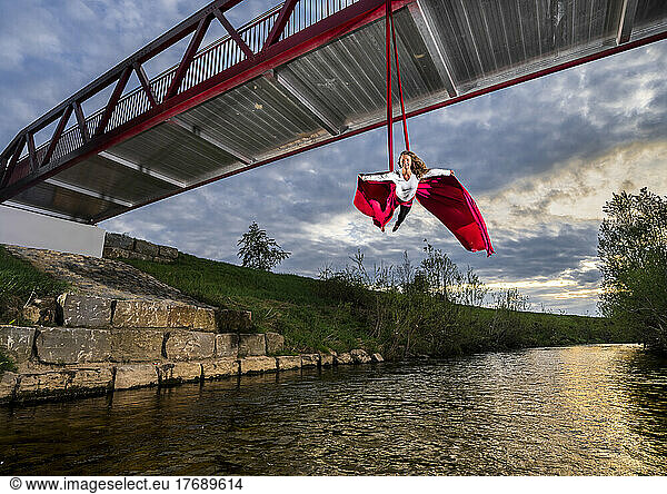 Athlete practicing aerial acrobatic hanging from bridge over Rems river