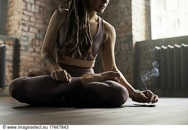 Athlete sitting cross-legged holding burnt incense stick in yoga studio