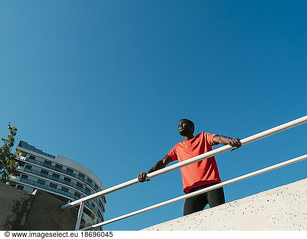 Athlete standing near railing under clear blue sky