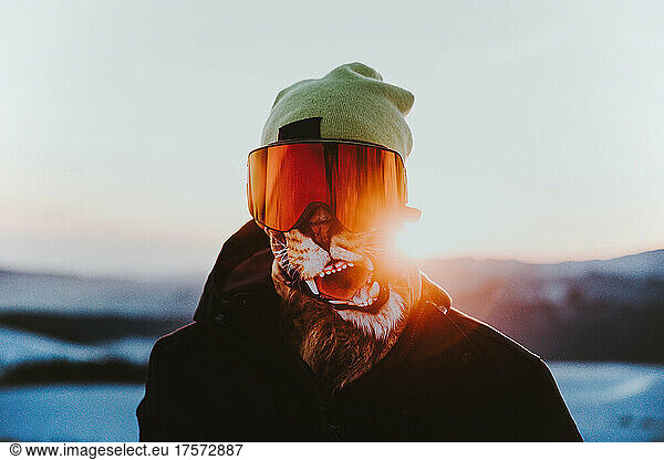 Athlete wearing buff goggles and snow jacket on the mountain at sunset