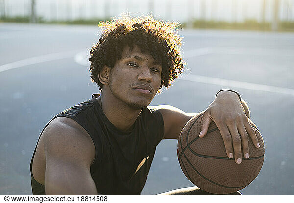 Athlete with curly hair holding basketball at court