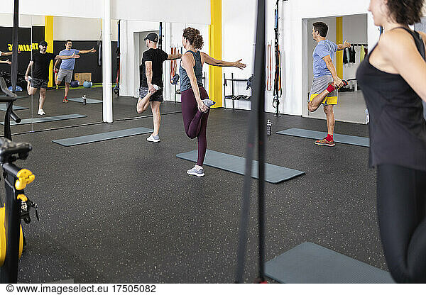 Athletes stretching on one leg exercising in front of mirror at gym