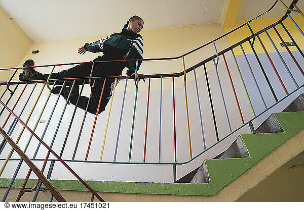 athletic androgynous strong woman balances on railing in colour school