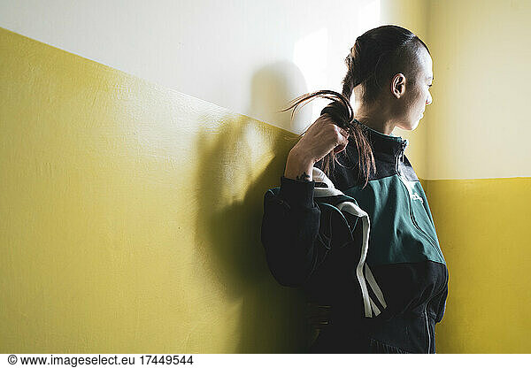 athletic androgynous strong woman coils hair in window light on yellow