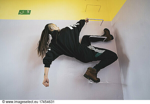 athletic androgynous strong woman hangs off bars in pastel school