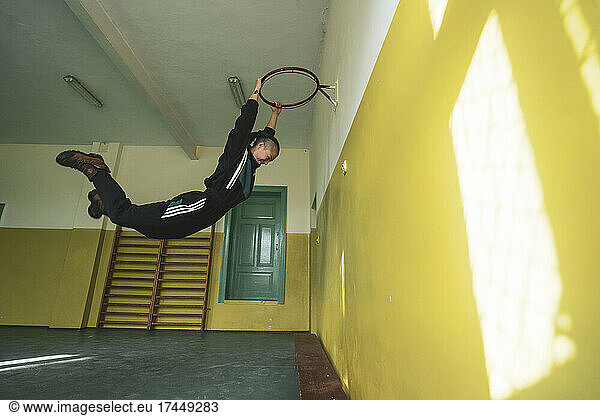 athletic androgynous strong woman hangs off basketball hoop in school