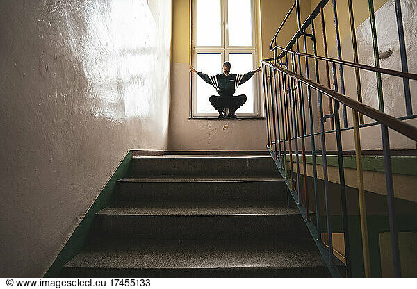 athletic androgynous strong woman sits in window of colourful school