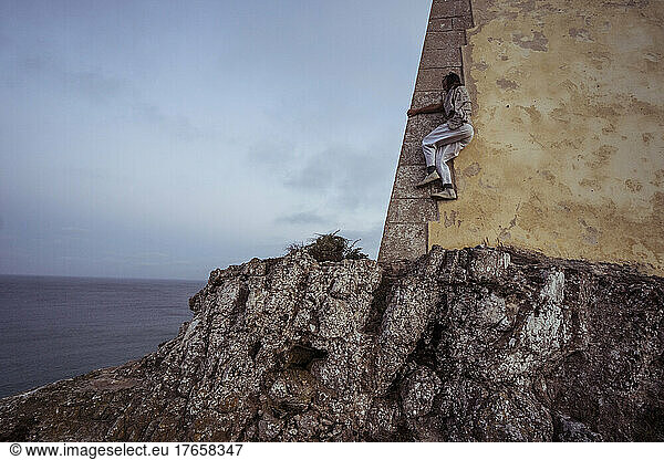 athletic dancer climbs fort wall on ocean cliff in Portugal