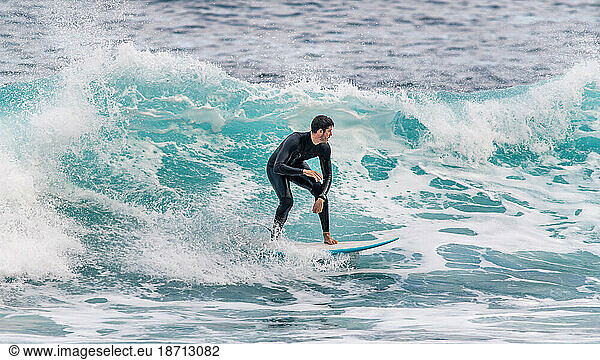 Athletic young man surfing a wave in a wetsuit in Tenerife
