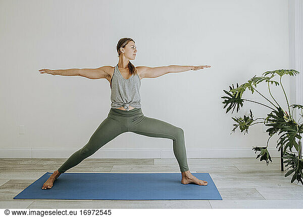 Athletische Frau macht Krieger-Yoga-Pose drinnen auf blauer Matte