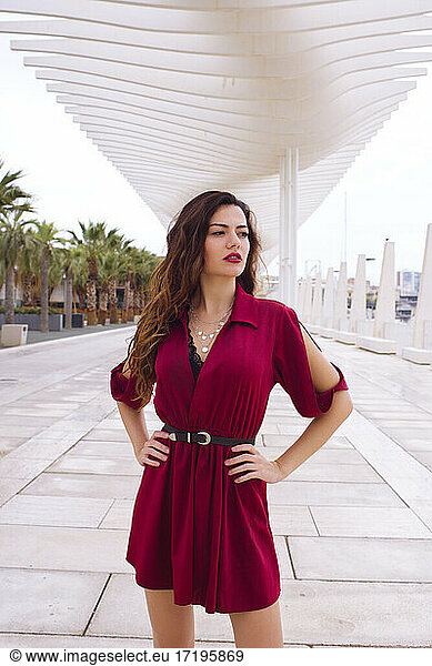 Attractive and pretty model poses with red dress on a city stree