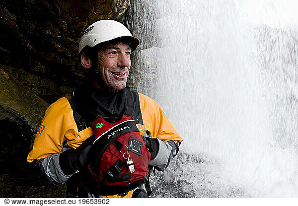 Attractive male kayaker standing underneath a waterfall.