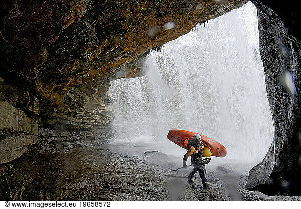 Attractive male kayaker standing underneath a waterfall.