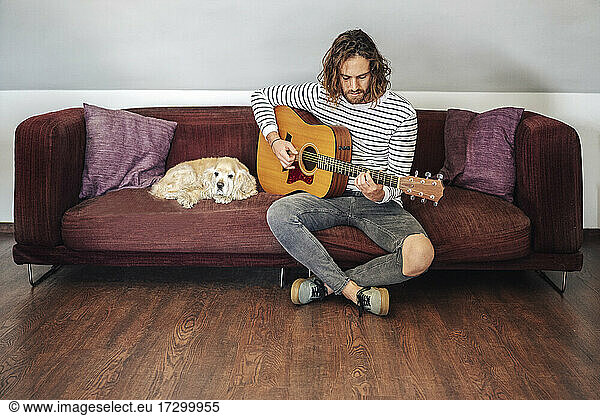 Attractive man with long hair playing acoustic guitar indoor with dog