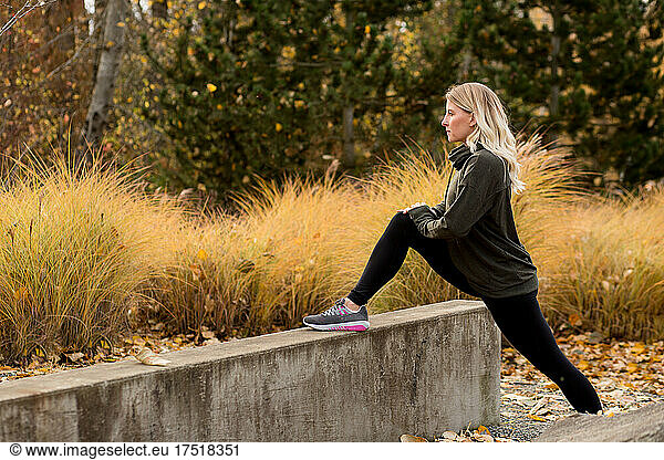 Attractive woman in fall workout gear stretches for a run
