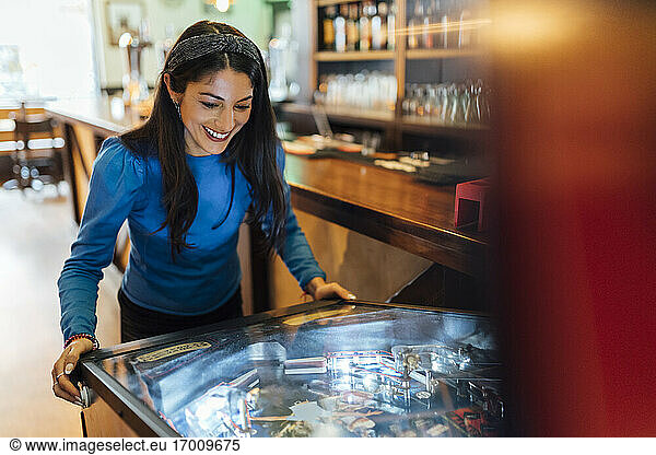 Attractive woman playing pinball in bar
