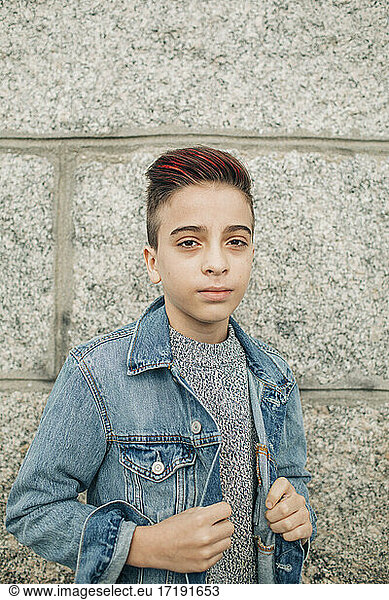 Attractive young boy with red highlights hair and denim by wall