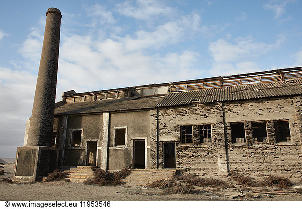 Außenansicht eines verlassenen Gebäudes und eines Industrieschornsteins.
