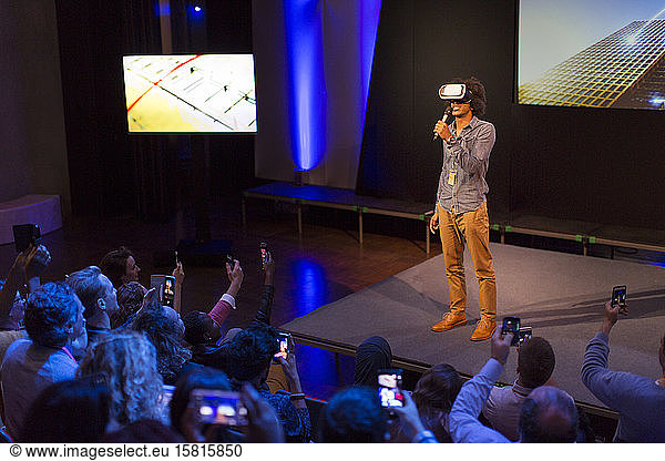 Audience watching male speaker with virtual reality simulator glasses on stage