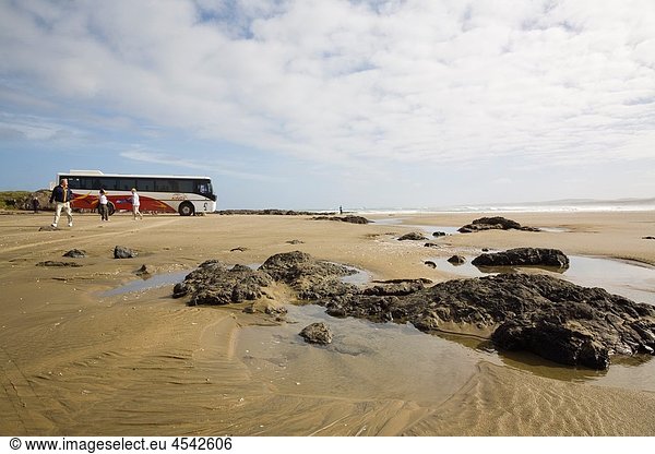 Aupori Peninsula Northland North Island New Zealand Remote Ninety Mile Beach with rocks water pool wet sand tourists and parked coach at The Bluff on Tasman sea coast