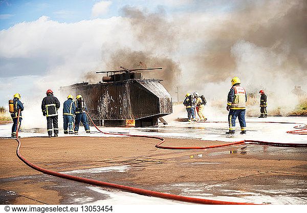 Ausbildung von Feuerwehrleuten  Team von Feuerwehrleuten sprüht Feuerlöschschaum am Scheinhelikopter in der Ausbildungsstätte