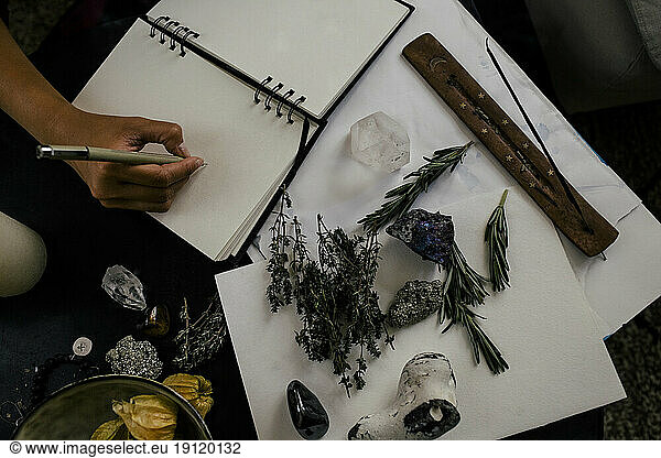 Ausgeschnittenes Bild einer Frau  die neben Kräutern und Kristallen auf einem Tisch in ein Buch schreibt