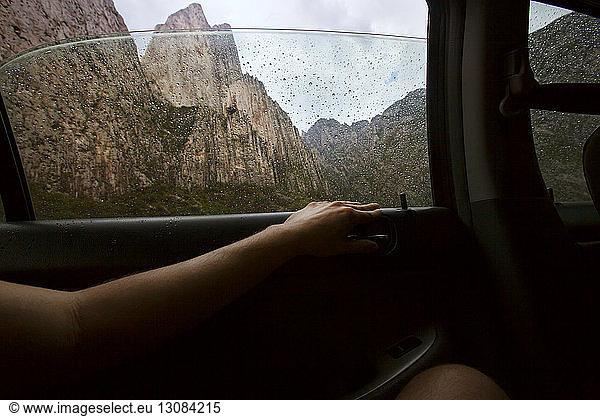 Ausgeschnittenes Bild einer im Auto sitzenden Person mit Bergen im Hintergrund