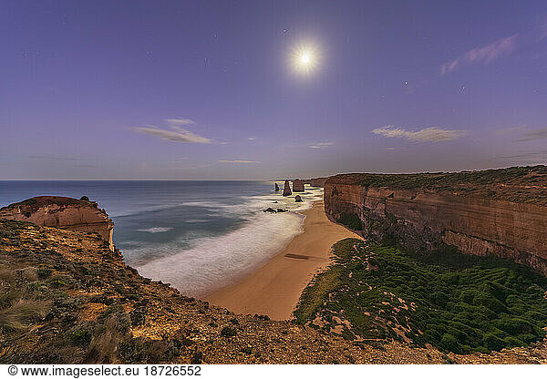 Australia  Victoria  Long exposure of moon glowing over sandy beach in Port Campbell National Park at night