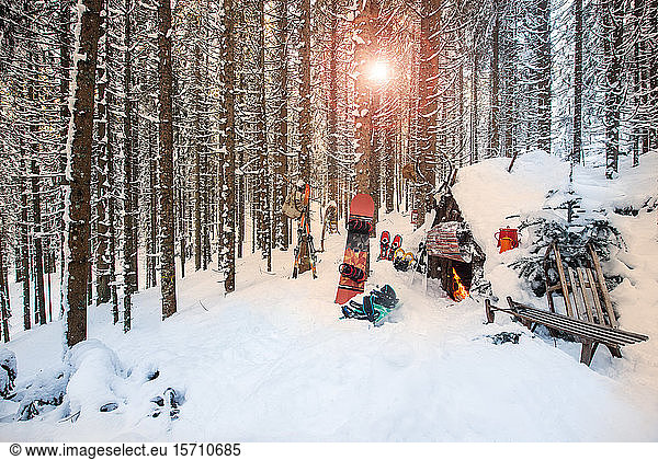 Austria  Salzburg  Altenmarkt im Pongau  Winter sports equipment lying in front of snow-covered forest hut at sunset