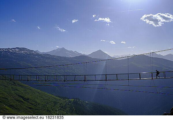Austria  Salzburg  Bad Gastein  Silhouette of person crossing suspension bridge stretching over Gastein Valley