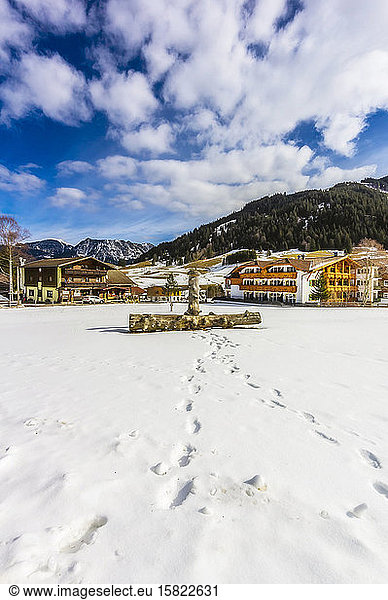 Austria  Tyrol  Tannheim  Footprints leading to wooden log lying in snow in front of town houses