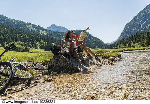 Austria  Tyrol  Tannheim Valley  young couple with mountain bikes and map sitting at brook