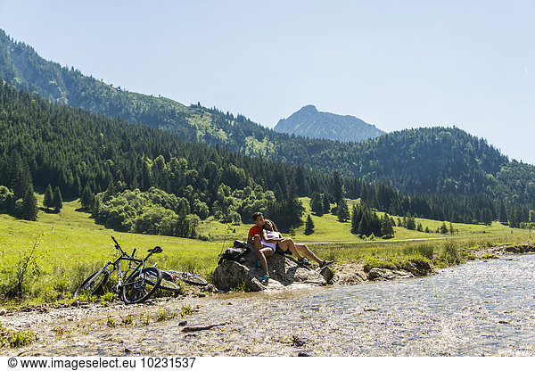 Austria  Tyrol  Tannheim Valley  young couple with mountain bikes relaxing at brook