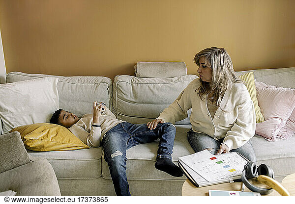 Autistic son lying on sofa by mother in living room