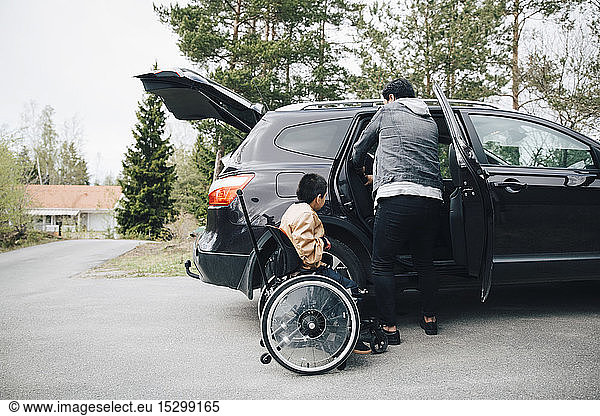 Autistic son waiting by father adjusting car seat on driveway