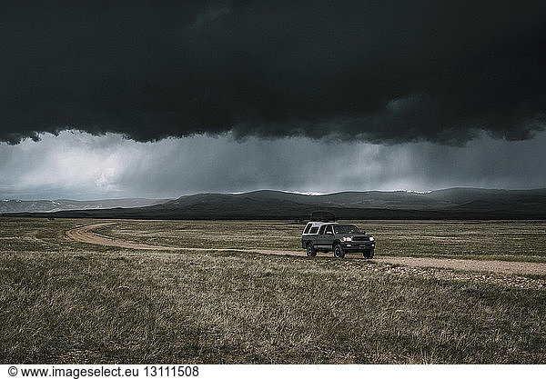 Auto auf unbefestigter Straße gegen dunkle Gewitterwolken