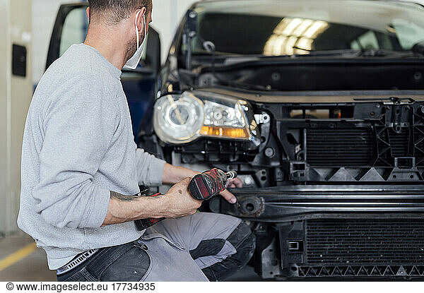 Auto mechanic repairing car with electric screwdriver in workshop