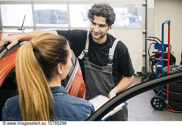 Automechaniker im Gespräch mit Kunden in der Werkstatt