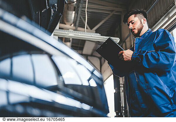 Automechaniker schreibt Reparaturplan auf Klemmbrett. Autoservicemitarbeiter männlich