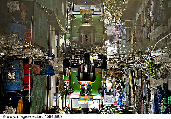 Autorikscha spiegelt sich in einer Pfütze in einer Bangkoker Gasse