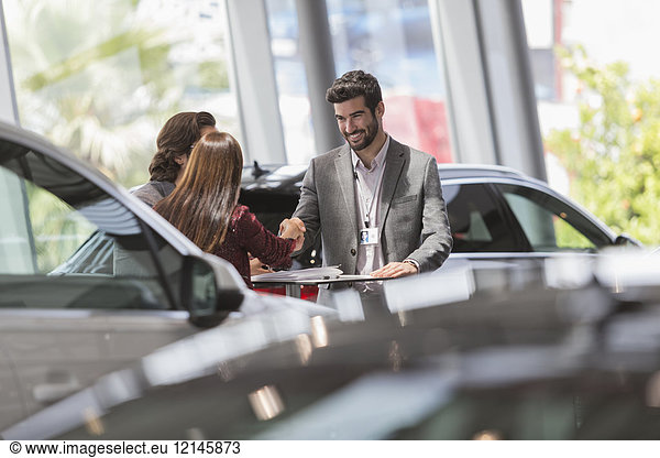 Autoverkäufer beim Händeschütteln mit Kunden im Autohaus-Showroom