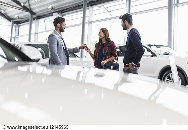 Autoverkäufer übergibt Autoschlüssel an Kunden im Autohaus-Showroom