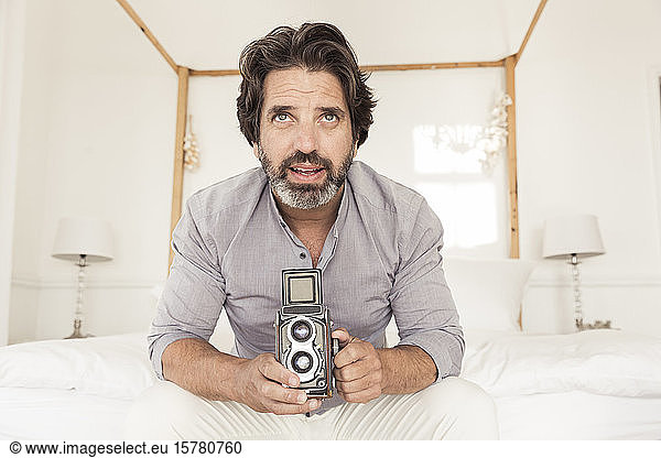 Bärtiger Mann auf Bett sitzend mit altmodischer Kamera