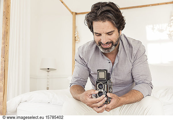 Bärtiger Mann auf Bett sitzend mit altmodischer Kamera