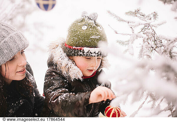 Baby boy and his mother decorating Christmas tree outdoors in winter