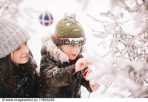 Baby boy and his mother decorating Christmas tree outdoors in winter