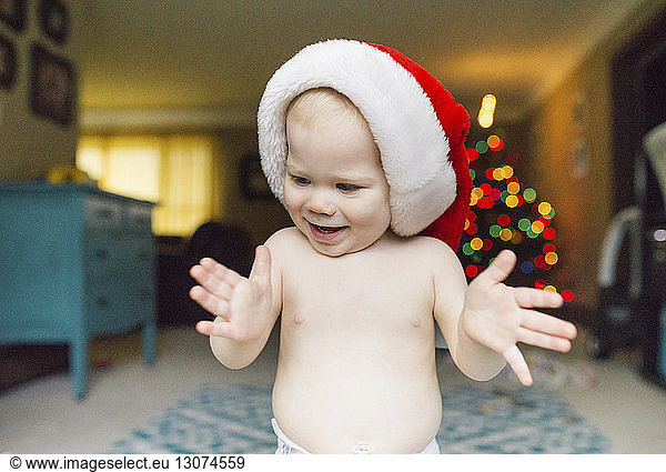 Baby boy in Santa hat clapping while standing at home