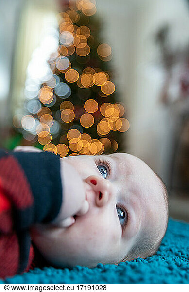 Baby boy laying near Christmas tree.