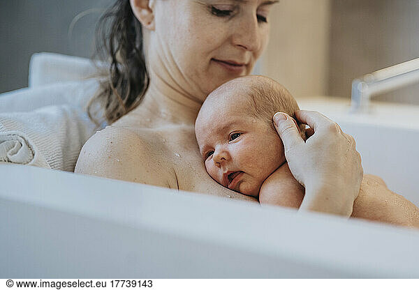 Baby boy lying on mother's chest in bathtub at home