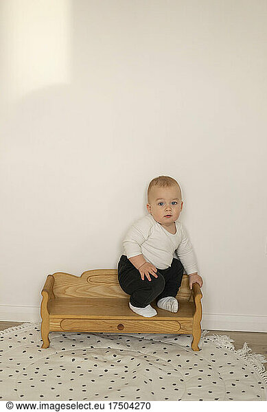 Baby boy sitting on seat near wall at home